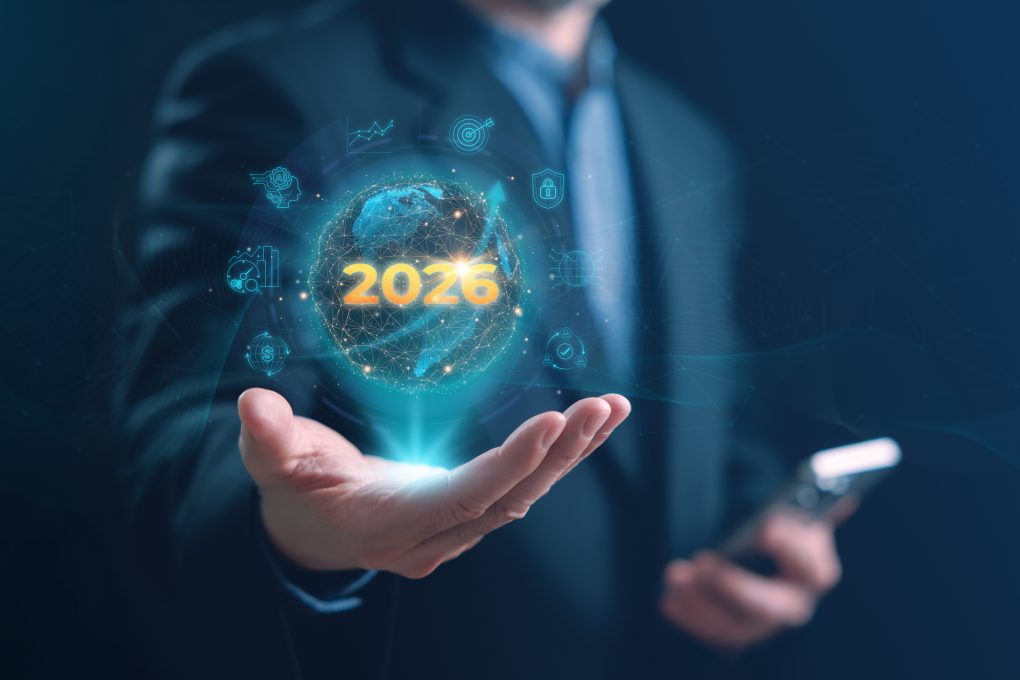 A businessman holding a glowing holographic globe with 2026 surrounded by business growth, strategy, analytics, and innovation icons, representing future development and data-driven business success.